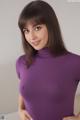 A woman in a purple turtleneck is posing for the camera.