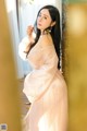 A woman in a pink dress leaning against a wall.