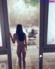 A naked woman standing in front of a glass door.