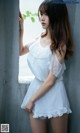 A woman in a white dress leaning against a wall.