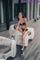 A woman in a black bikini sitting on a white chair.