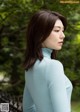 A woman in a blue turtle neck sweater standing in front of a fence.