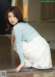 A woman in a blue sweater and white skirt crouching down.