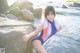 A woman in a bathing suit leaning against a rock by the ocean.