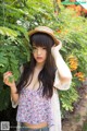 A woman wearing a straw hat standing in front of a bush.