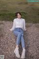 A woman in a white shirt and jeans sitting on a gravel road.