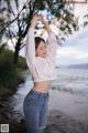 A woman in a white sweatshirt and jeans standing on a beach.