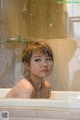 A woman sitting in a bathtub with water droplets on her face.