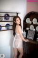 A woman in a white lingerie posing in front of a dresser.