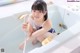 A woman sitting in a bathtub holding a shower head.