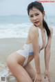 A woman in a white bikini sitting on the beach.