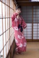 A woman in a red and white kimono standing by a window.