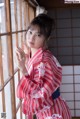 A woman in a red and white kimono leaning against a window.