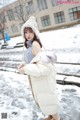 A woman in a white coat and hat standing in the snow.