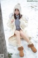 A woman sitting in the snow wearing a white coat and hat.