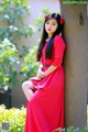 A woman in a red dress leaning against a tree.