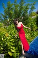 A woman in a red dress standing next to a swimming pool.