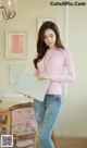 A woman in a pink sweater and jeans holding a laptop.