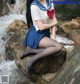 A woman in a sailor outfit sitting on a rock by a stream.