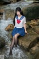 A woman in a sailor outfit sitting on a rock by a stream.