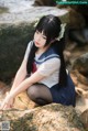 A woman in a school uniform sitting on a rock by the water.