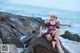 A woman in a purple bikini sitting on a rock by the ocean.