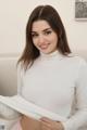 A woman in a white turtle neck sweater is posing for the camera.