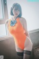 A woman in an orange bodysuit and black stockings posing for a picture.