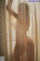 A naked woman standing in front of a window.