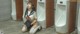 A woman in a sailor outfit sitting on the floor next to urinals.