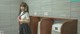 A woman in a school uniform standing next to a urinal.