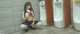 A woman in a school uniform crouching down in front of urinals.