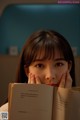 A young woman holding a book in front of her face.